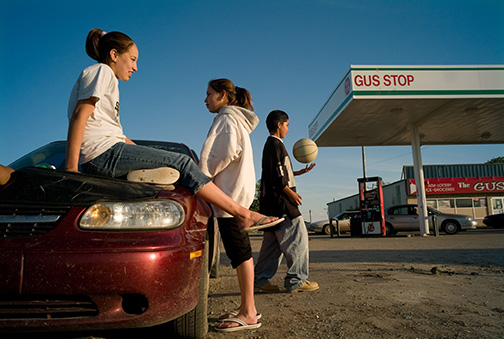 Teens Ariel Farmer, 14, left, Kyla Sharp Butte, 14, center, and Will Sharp Butte, 15, hang out on the hood of a car in the parking lot of a convenience store to pass time on the Rosebud Sioux Reservation in southern South Dakota, Thursday, May 24, 2007. An epidemic of teen suicides and attempts has reservation adults worried. Making these images caused a worried father — even one to whom I had introduced myself — call the tribal police. © Kevin Moloney, 2007.